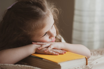 Cute little girl laid her head on a yellow book at home. The idea of a child’s activity in quarantine