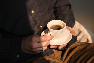 Stylish man with a cup of coffee. Businessman is drinking morning coffee after breakfast. Delicious hot espresso in white cup. Enjoy moment, take break. Freelancer lifestyle. Morning sun in the room