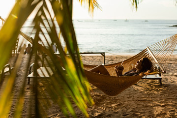 Woman relaxing on the hammock on the beach at sunset