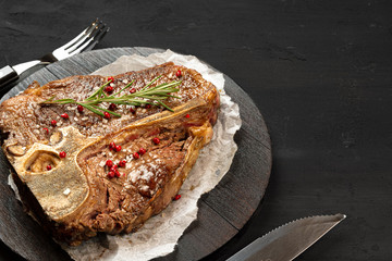 Top view of grilled t-bone steak with spices on black table