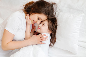 Happy young mother hugs her little daughter in bed, a view from above. mother and daughter rest in bed at home. Good morning!