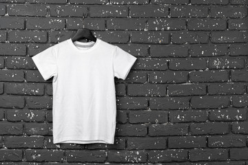 White t-shirt hanging on hanger against brick wall, copy space