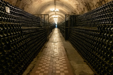 A long antique cellar with lots of aged wine bottles. Sparkling wine production