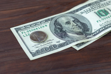 Wooden background in a dark style. On it are banknotes one hundred dollars and one ruble. Exchange rate and exchange operations.