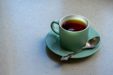 A pale green tea pair on a light artificial stone countertop. The Cup is filled with strong freshly...