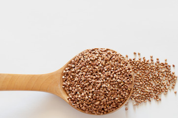 Sprinkled buckwheat in a wooden spoon on a white background. Copy space.
