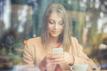 Happy girl using phone in coffee shop, through window view