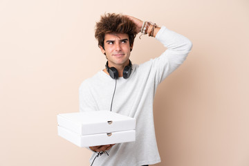 Young handsome man holding a pizza over isolated wall having doubts and with confuse face expression