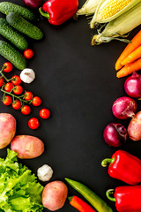 Set of autumn vegetables - potato, cucumber, carrot, greenery - on black background top-down copy space