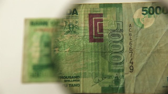 Five thousand Ugandan shillings and a magnifying glass. View a paper bill through a magnifying glass. Obverse.