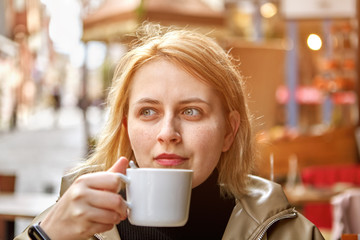 Young white woman drinks  coffee outside.