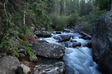 Obraz premium Rocky Mountain waterfalls and streams with smooth flowing water over boulders in pine trees