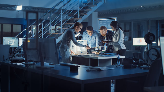 Diverse Team Of Electronics Development Engineers Standing At The Desk With 3D Printer And PCB Motherboards. Specialists Working On Ultra Modern Industrial Design, Using Advanced Technology