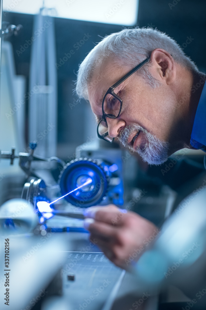 Fototapete Close-up Portrait of Focused Middle Aged Engineer in Glasses Working with High Precision Laser Equipment, Using Lenses and Testing Optics for Accuracy Required Electronics