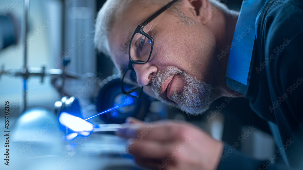 Poster Close-up Portrait of Focused Middle Aged Engineer in Glasses Working with High Precision Laser Equipment, Using Lenses and Testing Optics for Accuracy Required Electronics