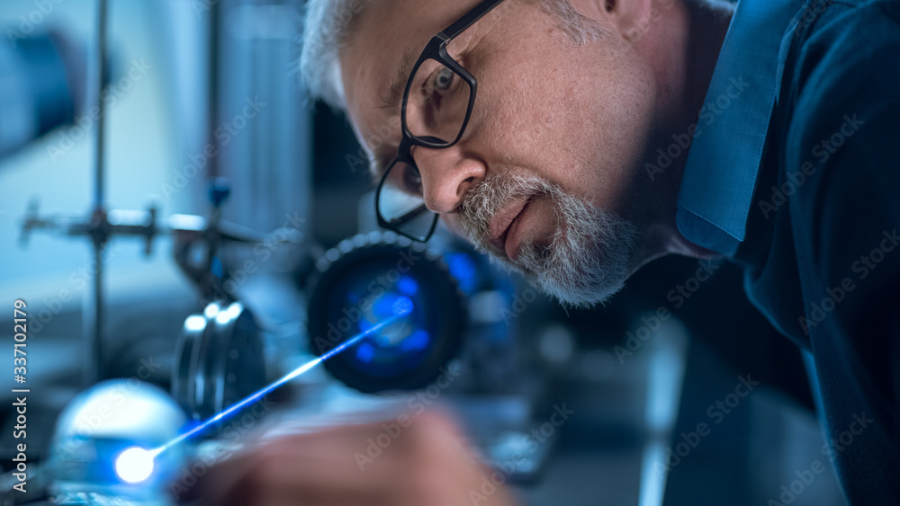 Poster Close-up Portrait of Focused Middle Aged Engineer in Glasses Working with High Precision Laser Equipment, Using Lenses and Testing Optics for Accuracy Required Electronics