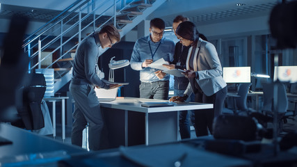 Diverse Team of Electronics Development Engineers Standing at the Desk Successfuly Solving Project Problems Late at Night. Specialists Working on Ultra Modern Industrial Design.