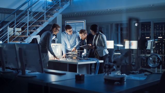 Team Of Electronics Development Engineers Standing At The Desk With 3D Printer And PCB Motherboards. Specialists Working On Ultra Modern Industrial Design, Using Advanced Technology.