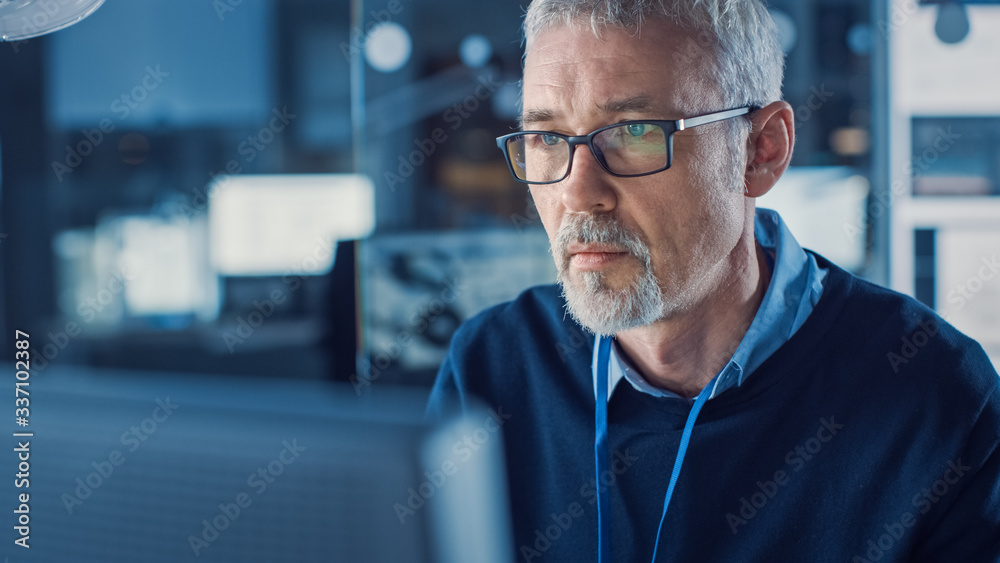 Poster portrait of handsome middle aged engineer wearing glasses works on personal computer. in the backgro