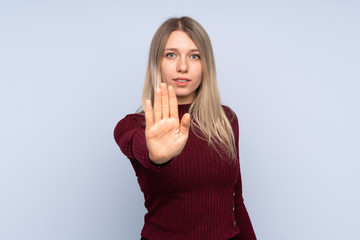 Young blonde woman over isolated blue background making stop gesture