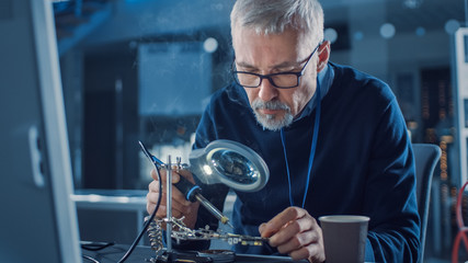 Electronics Maintenance Engineer Enters His Workshop with Coffee Beginss Soldering of Circuit...