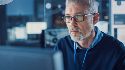 Portrait of Handsome Middle Aged Engineer Wearing Glasses Works on Personal Computer. In the...