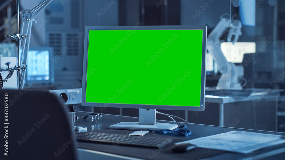 Aufkleber On the Desk Computer with Isolated Green Mock-up Screen Display. In the Background Robot Arm Concept Standing in Heavy the Dark.Industry Engineering Facility