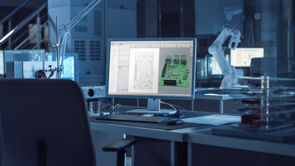  On the Desk Computer With CAD Software and Design of 3D Industrial Machinery Component. In the Background Robot Arm Concept Standing in Heavy Dark. Industry Engineering Facility.
