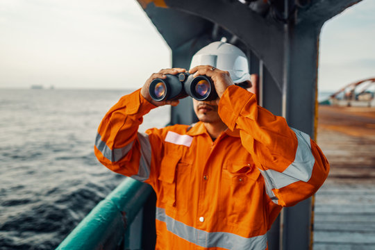 Filipino deck Officer on deck of vessel or ship , wearing PPE personal protective equipment. He is looking through binoculars.