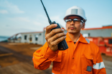 Filipino deck Officer on deck of vessel or ship , wearing PPE personal protective equipment. He holds VHF walkie-talkie radio in hands. Dream work at sea