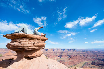 Office worker reclining outdoors with a tablet on mesa rock above a dramatic canyon landscape