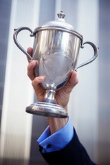 Hand of proud unrecognizable businessman holding up a silver trophy outdoors in front of shiny modern office building