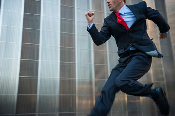 Unrecognizable businessman jumping outdoors in motion blur across modern urban office building background