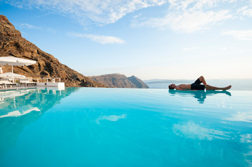 Solitary young man resting on the edge of an infinity pool overlooking a scenic Mediterranean view of the Santorini caldera, Greece