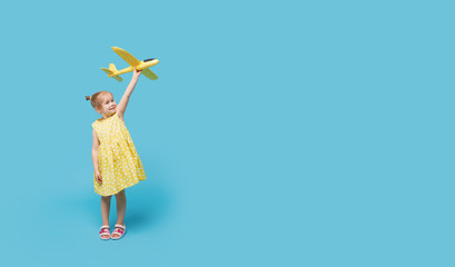 Little girl child in a summer dress holds in his hands a toy airplane on a blue background. Time to travel