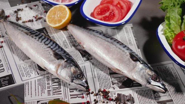 Fresh mackerel on a stylish vintage newspaper. Next to fresh bread, seasoned with onions, pickles, tomato and herbs and pepper. Slider shot. Top view. Close up.