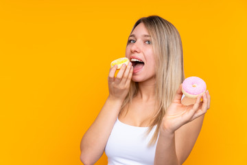 Young blonde woman over isolated blue background eating a donut