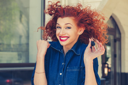 Just won an apartment!!! Super excited Smiling red head curly girl holding showing keys to her new home isolated near apartment complex outdoors. Business woman real estate agent renting agent concept
