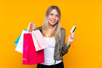 Young blonde woman over isolated yellow background holding shopping bags and a credit card