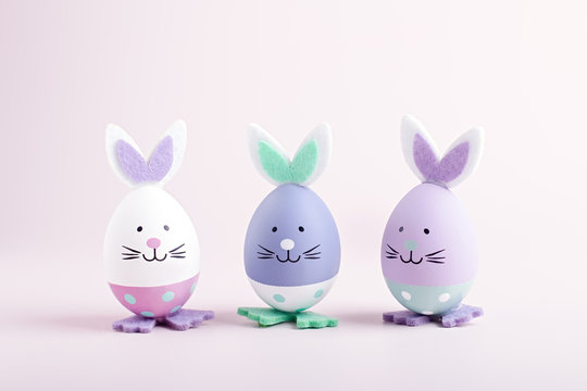 Funny kawaii cute bunny eggs close up for kids in pastel colors on pink table top, Easter holiday concept. Easter decoration for kids still life, copy space