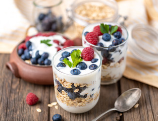 White yogurt in three jars with raspberries and blueberries on natural wooden background.