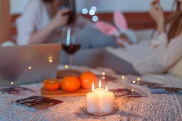 Two girl friends arranged a romantic cozy dinner with wine on the sofa in the apartment during self isolation and quarantine