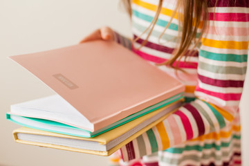 Close up of child schoolgirl holding colorful books in her hand,  education, learning at home, self-study