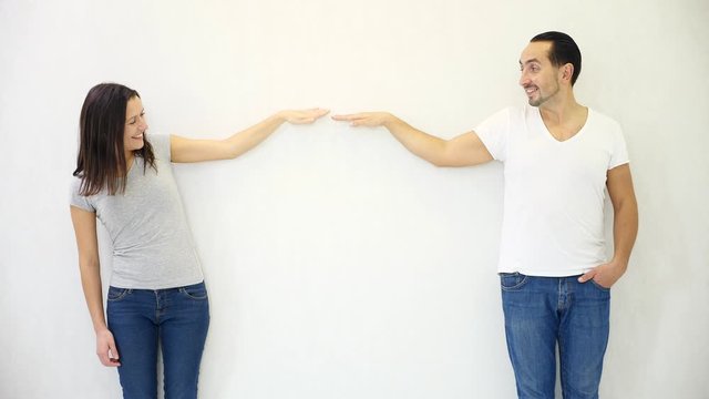 Brunette man and woman standing against white wall background and lowering their hands, showing loss and dicrease of something.