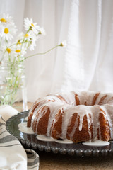 Lemon Ricotta Bundt Cake with icing displayed on a black decorative plate in a light bright airy setting.