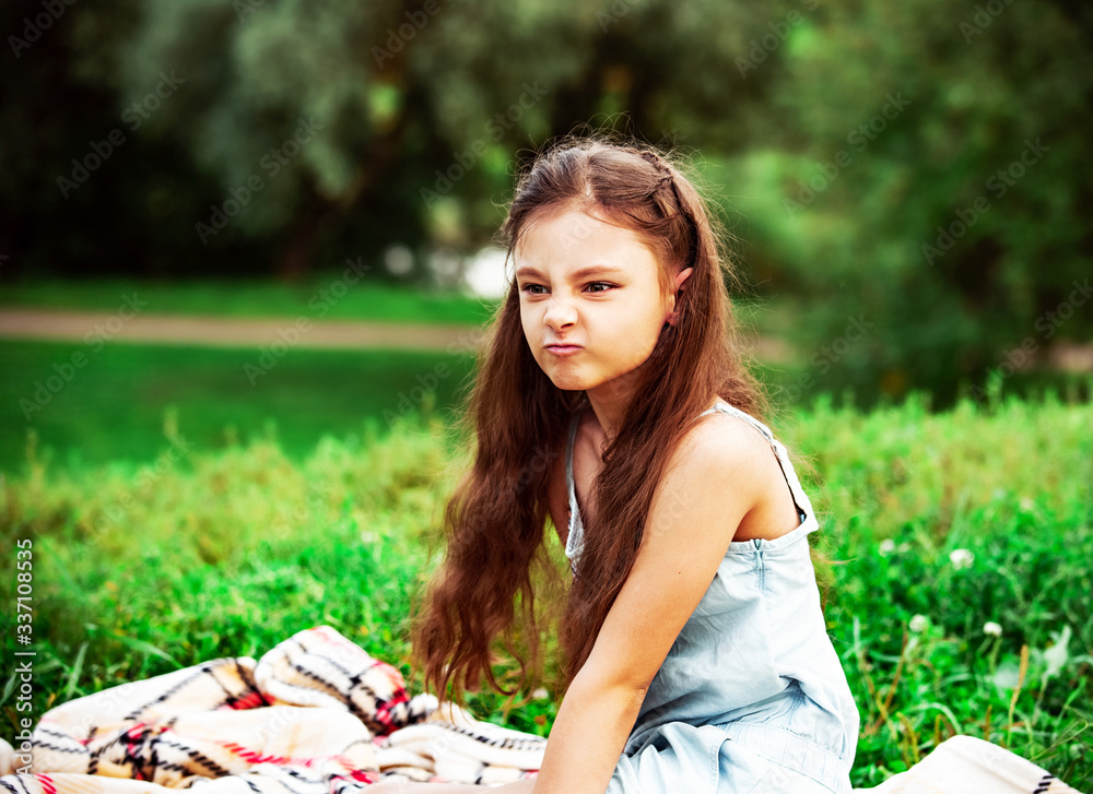 Wall mural angry grimacing unhappy kid girl long hair on summer green grass background. closeup