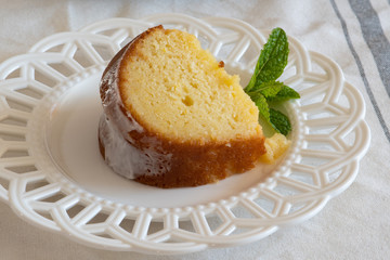 A slice of moist Lemon Ricotta Bundt Cake on a white decorative plate with a mint leaf garnish.