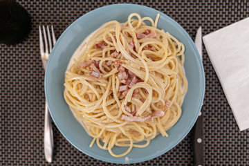 Spaghetti Carbonara served on a blue plate with fork and knife