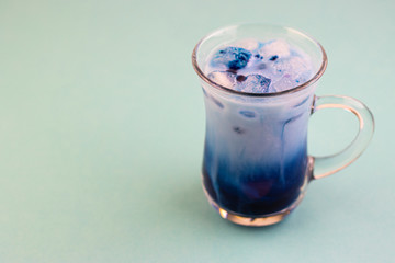 Blue matcha tea with milk and ice cubes in a glass of latte on a blue table