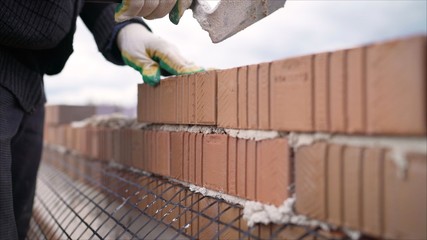 Worker in Close up of industrial bricklayer installing bricks and mortar cement brick on construction site. Worker builds a house of colored brick.